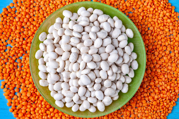 Top view white beans in a green plate and red lentils on a blue wooden background.