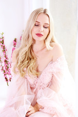 Young beautiful woman with blond wavy hairstyle wearing tender pink wedding dress. Fragile bride portrait in full length maxidress. Close up, copy space, background.