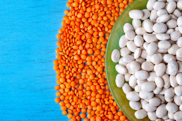 Top view white beans in a green plate and red lentils on a blue wooden background.