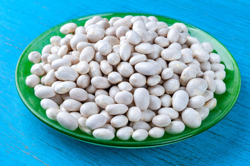 White beans in a green plate on a blue wooden background.