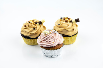 Three great and delicious muffins filled with caramel and strawberry foam. Decorated with a sweet tube. Isolated on white background.