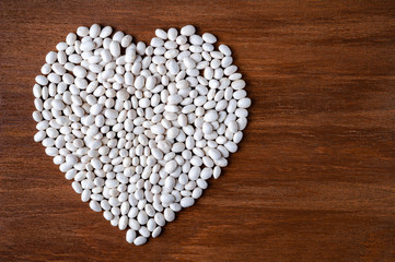 Many white beans poured into the shape of a heart on a wooden background.