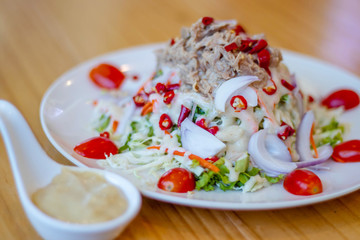 Spicy tuna salad In a white plate, salad this dish consist of tuna, lettuce, chinese cabbage, carrot onion red chilli rough cut, and tomato half cut Used to arrange dishes dressing in a spoon ceramic.