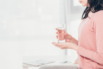 Cropped view of woman holding glass of water at home with copy space
