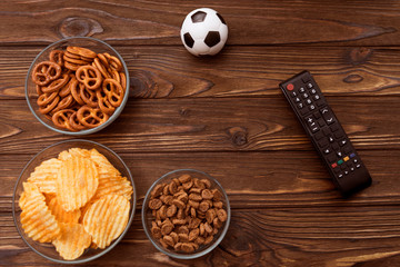 Chips, crackers, snacks, TV remote control, soccer ball on wooden table background. football match, fans. sport.