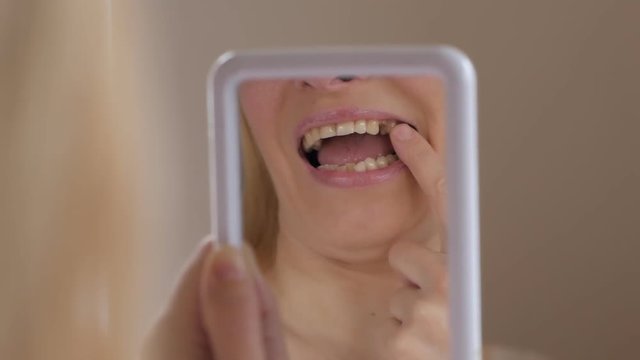 Close-up of the face of an adult woman examining in the mirror missing tooth in the mouth.