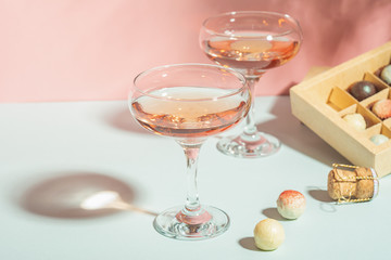 Champagne or wine in glasses box of chocolates of white and dark chocolate on pink background bright light. Copy space.