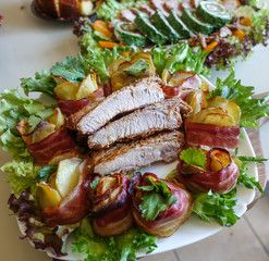Grilled pork ribs on a white plate with greens, lettuce and meat rolls