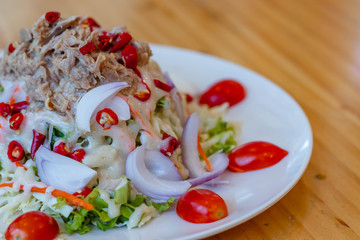 Spicy tuna salad In a white plate, salad this dish consist of tuna, lettuce, chinese cabbage, carrot onion red chilli rough cut, dressing and tomato half cut Used to arrange dishes.