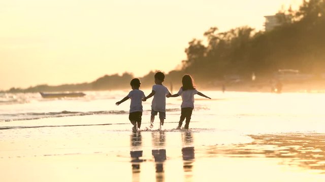 brother and sisters are holding hand together with happiness while playing at the beach during sunset time. happy family concept.
