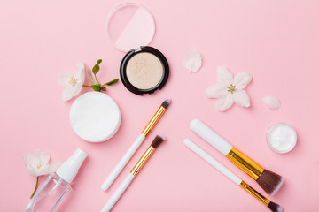 Obraz na płótnie Canvas Face care and make up products with spring apple bloom (tonic or lotion, serum, cream, micellar water, cotton pads and makeup brushes) on pink background. Freshness and face care. Decorative cosmetics