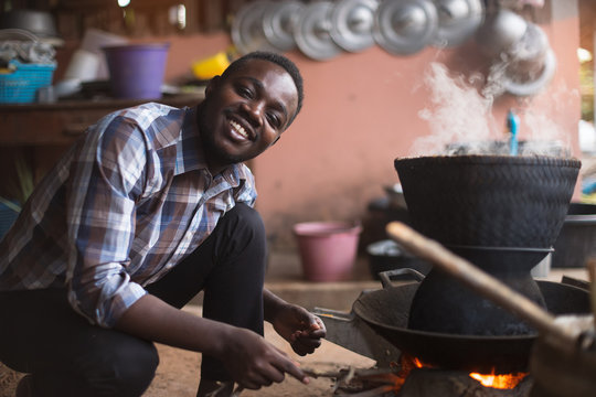 African man sitting to blow fire to cook rice
