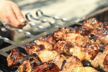 Meat skewers on grill and man hand as background, closeup. Outdoor kitchen