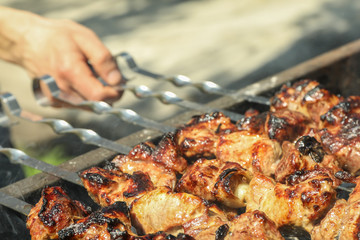Meat skewers on grill and man hand as background, closeup. Outdoor kitchen