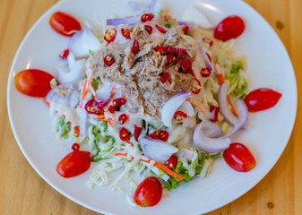Spicy tuna salad In a white plate, salad this dish consist of tuna, lettuce, chinese cabbage, carrot onion red chilli rough cut, dressing and tomato half cut Used to arrange dishes.