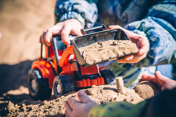 little child playing with a red excavator in a sandbox