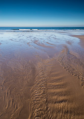 A tranquil scene of the sandy beach at Bamburgh, Northumberland, England UK with a stream flowing towards the sea.
