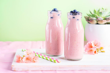 Pink milk shake in glass bottles topped with blueberries. Pink flowers and colorful straws.