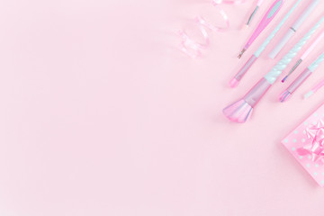 Feminine accessories with unicorn makeup brushes on pink background and a polka dot festive gift envelope. Flat lay with copy space, birthday beauty and cosmetics blogger concept