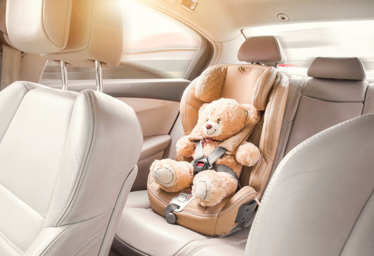 Baby child seat car. A beige teddy bear is fastened with seat belts in a car seat. Travel by car