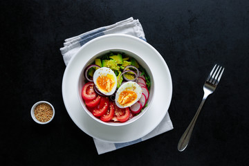 healthy bowl fresh salad with boiling egg  tomatoes avocado radish arugula red onion sesame seeds fork napkin    on black background top view 