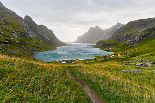 Hiking trail leading to a beautiful bay surrounded by mountains and a small village near Bunes Beach and Vinstad on Lofoten Islands in Norway