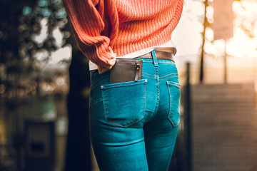 View from behind of a woman wearing tight jeans and an orange blouse with a brown leather wallet...