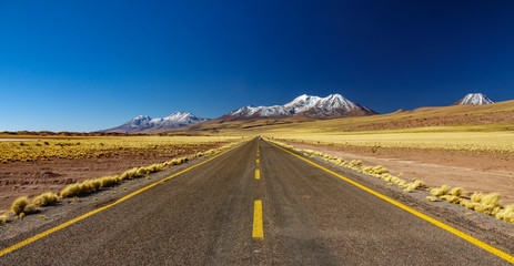 Atacama straight road against snow covered volcanoes