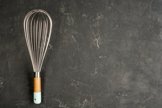 Kitchen Wire Whisk Eggs Beater on the dark concrete background with copy space. Flat lay background.