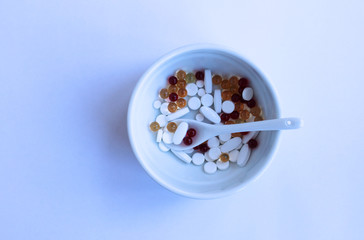 Red, white and yellow vitamin capsules and tablets in a white plate on a white background.