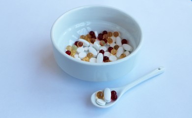 Red, white and yellow vitamin capsules and tablets in a white plate on a white background.