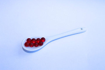 Red vitamin capsules in a white spoon on a white background.