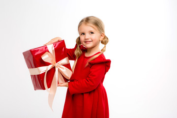 Portrait of little girl in red dress on isolated white background. Smiling Girl in shirt with gifts in hands looking at camera. Isolated gray background. The concept of celebrating, giving and receivi