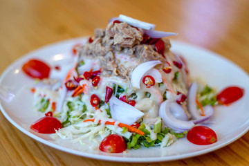 Spicy tuna salad In a white plate, salad this dish consist of tuna, lettuce, chinese cabbage, carrot onion red chilli rough cut, dressing and tomato half cut Used to arrange dishes.