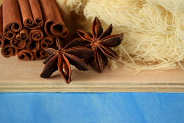 Anise stars, cinnamon sticks and kataifi dough on the wooden board against the blue background