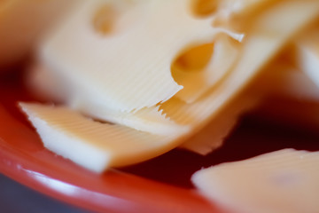 Fototapeta na wymiar Close-up of several slices of cheese with large holes on a red saucer