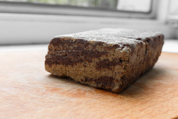 slice of sunflower halva with chocolate on the wooden cutting board, selective focus