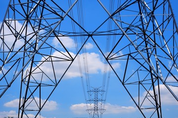 Selective focus of high voltage towers with cable lines against cumulus clouds and blue sky background in sunny day,  low angle view