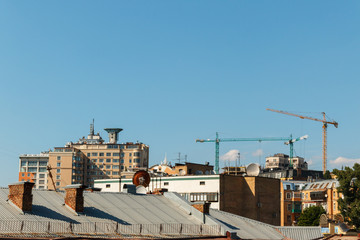 cityscape with roofs of houses and three construction cranes on the blue sky background with space for text. Turret slewing cranes, old and new architecture in Kyiv.