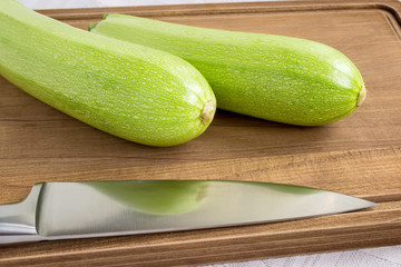Two fresh green courgettes or zucchini and professional chef knife on a brown wooden cutting board. Cook at home. Fresh vegetables, vegetarianism and healthy food.