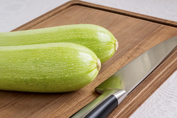 Two fresh green courgettes or zucchini and professional chef knife on a brown wooden cutting board. Cook at home. Fresh vegetables and healthy vegetarian food.