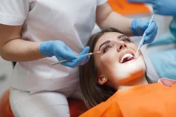 Foto auf Acrylglas Zahnärzte Zahnarztklinik. Empfang, Untersuchung des Patienten. Zahnpflege. Junge Frau unterzieht sich einer zahnärztlichen Untersuchung durch einen Zahnarzt. Glückliches Patienten- und Zahnarztkonzept. Zahnärztin in Zahnarztpraxis im Gespräch mit