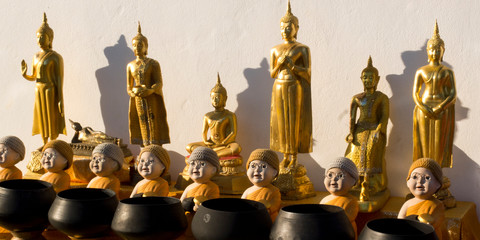 Fototapeta na wymiar Golden-coloured Buddhas in several postures : standing, sitting, and monk dolls before their charity bowls.