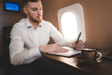 attractive and successful businessman in a white shirtt working sitting in the chair of his private jet.