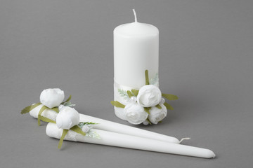 Three candles decorated with white roses on gray background.