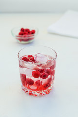 Refreshing drink with raspberries and ice. Lemonade on a white table, vertical orientation