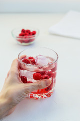Refreshing drink with raspberries and ice. Lemonade on a white table, vertical orientation