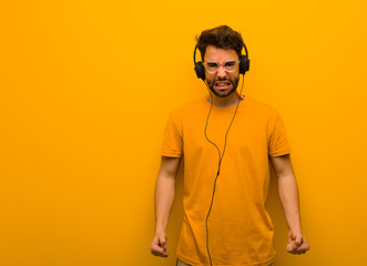 Young man listening to music screaming very angry and aggressive