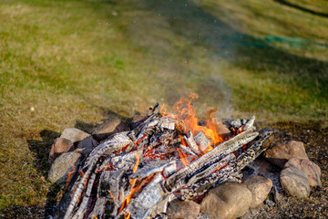open fire burning logs in field with green grass