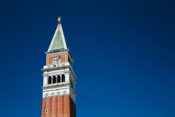 Fototapeta na wymiar Close up of the top of St Mark's Campanile bell tower, Campanile di San Marco on the blue sky background on St Mark's Square in Venice, Italy